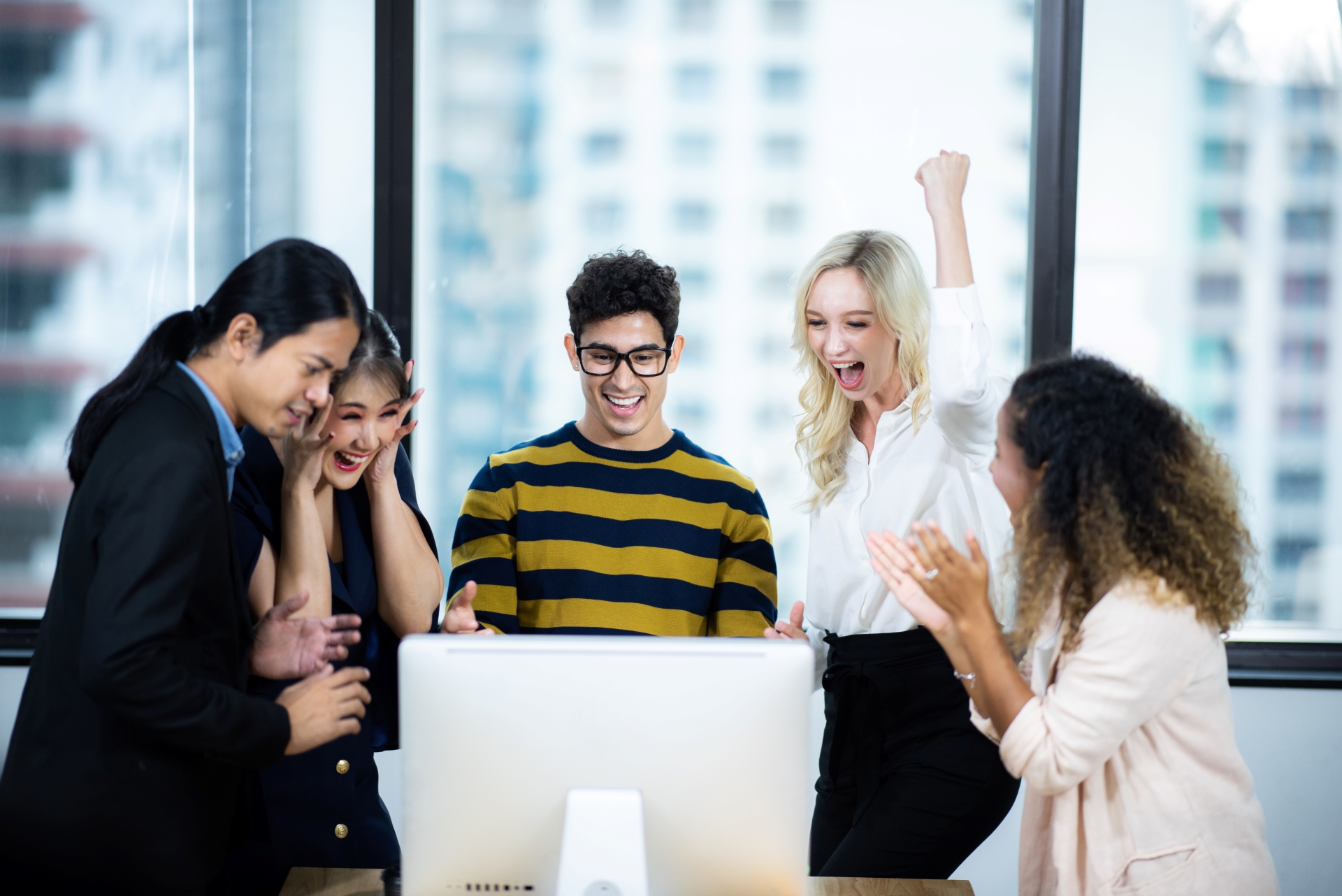 Diverse group of colleagues celebrating success in front of a computer.