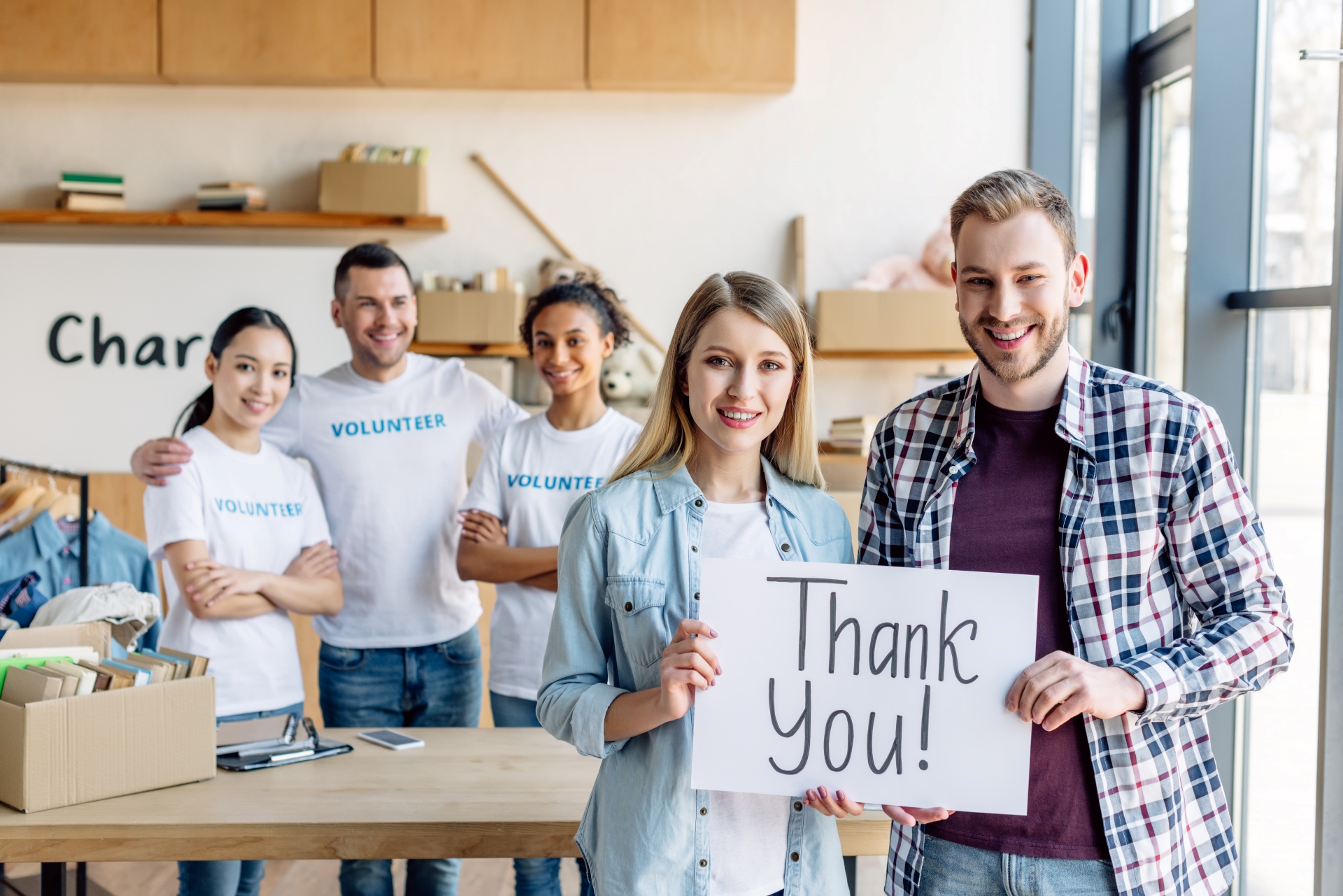 Group of happy volunteers holding a 'Thank You!' sign in a charity workspace.